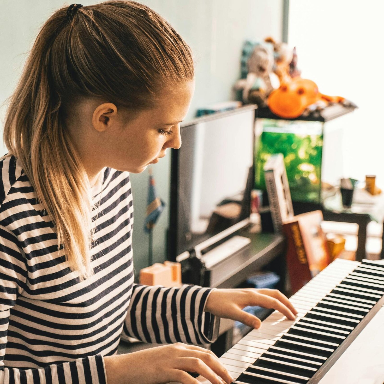A woman in a striped shirt playing a piano in a cozy indoor setting.